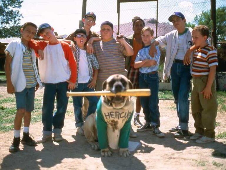 The Sandlot baseball team poses with Hercules the dog, who is wearing a jersey and holding a bat.