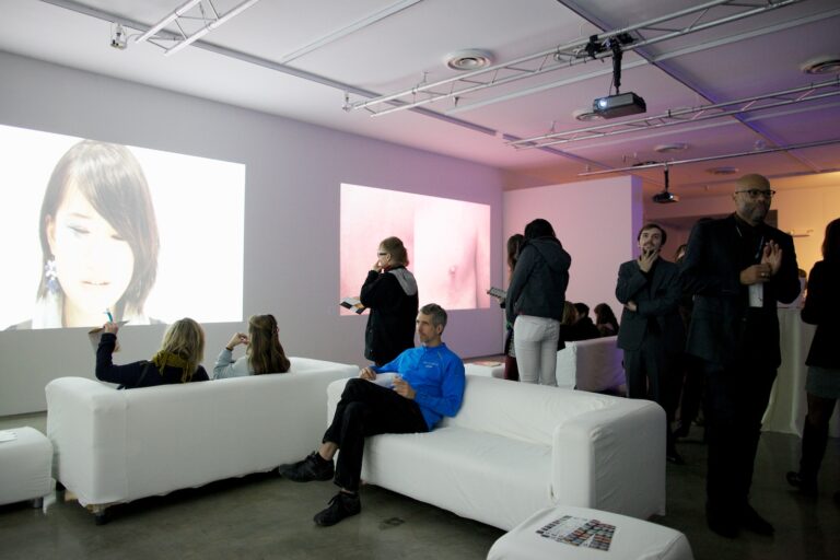 Art gallery showing projected images, people socializing. Digital media exhibit open to the public.