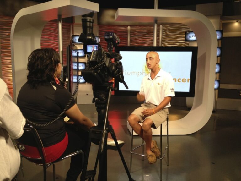Man being interviewed on TV, promoting "Triumph Over Cancer