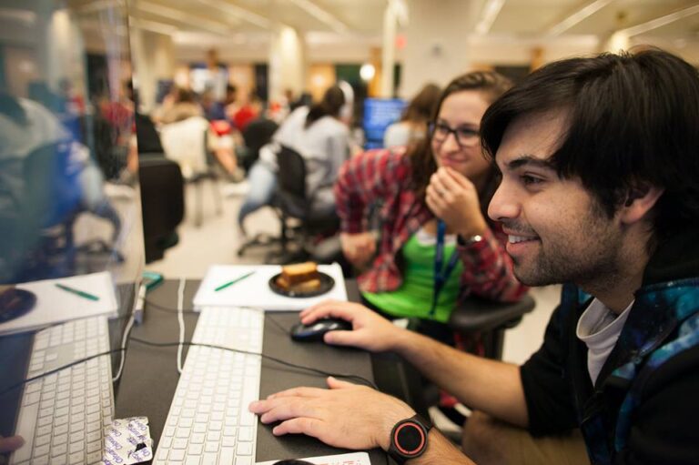 Two people working on computers in a busy office setting.