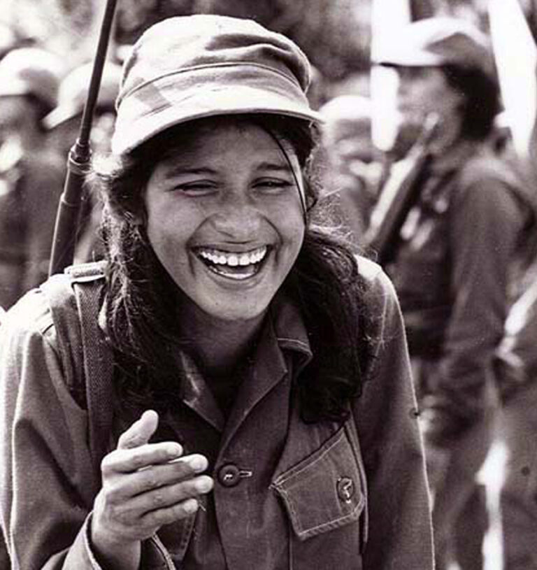 Smiling Sandinista woman soldier in uniform with rifle.