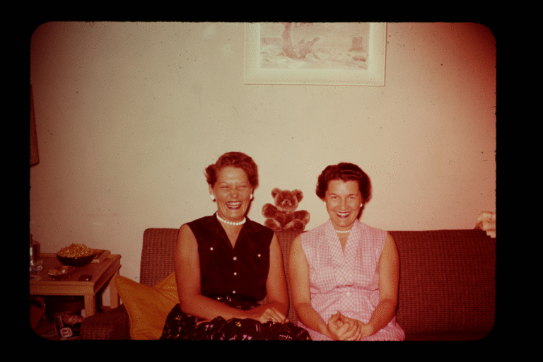 Two smiling women on a couch with a teddy bear, possibly related to 'A Secret Love' film discussion.