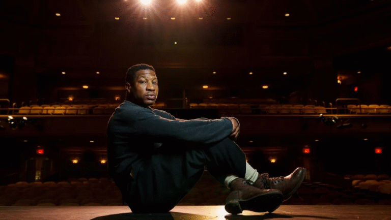 Jonathan Majors sitting on a stage in an empty theater.