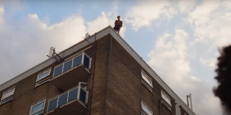 Person standing on the edge of a building in Andrea Arnold's 'Bird' film.