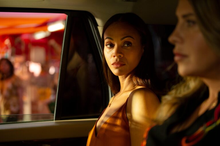 Zoe Saldana in 'Emilia Pérez' looking out car window with another woman, dramatic lighting.
