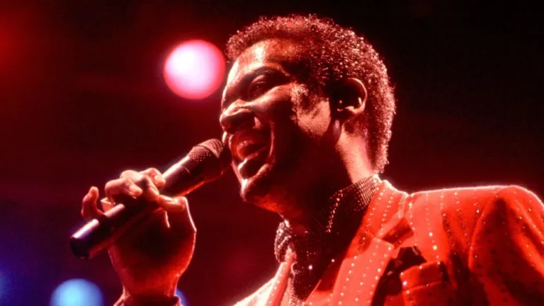 Luther Vandross performing live on stage, singing into a microphone with red lighting.
