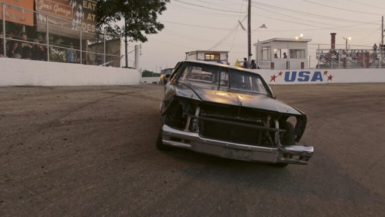 Demolition derby car on track, USA banner in background. "Joe's Garage: Eat at Joe's" sign visible.