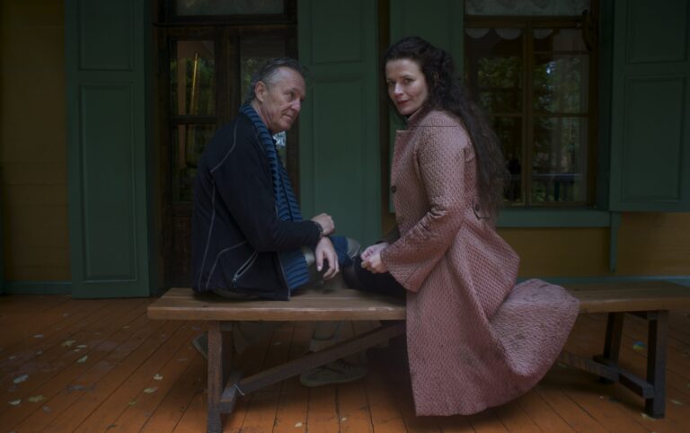 Man and woman sitting on a bench outside a green and yellow building.