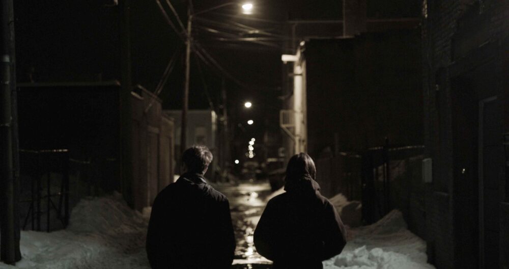 Two people walk down a snowy alley at night, evoking a sense of connection.