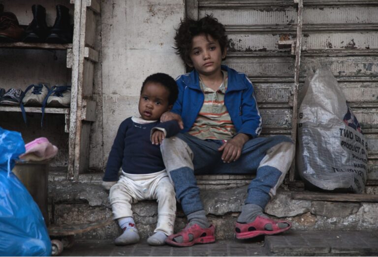 Two young boys sit on a stoop in Capernaum, looking somber.