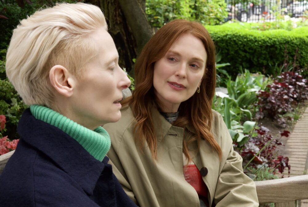 Tilda Swinton and Julianne Moore in "The Room Next Door" movie, sitting on a bench.