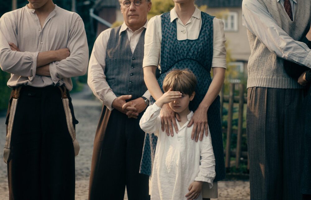 Family portrait evoking "Never Look Away": child shielding eyes, surrounded by relatives in vintage clothing.