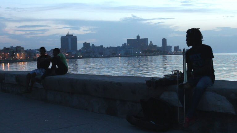 Musicians along the boardwalk in Havana, Cuba at dusk. City skyline in the background.