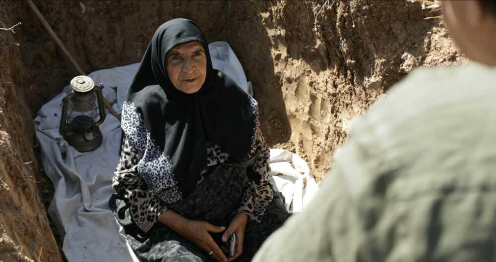 Elderly woman in a grave with a lantern, looking at someone.