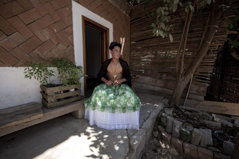 Person in traditional dress sitting outside, possibly related to "La Utopía De La Mariposa.