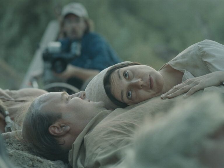 Couple lying down, possibly depicting a dead marriage, with a camera operator in the background.