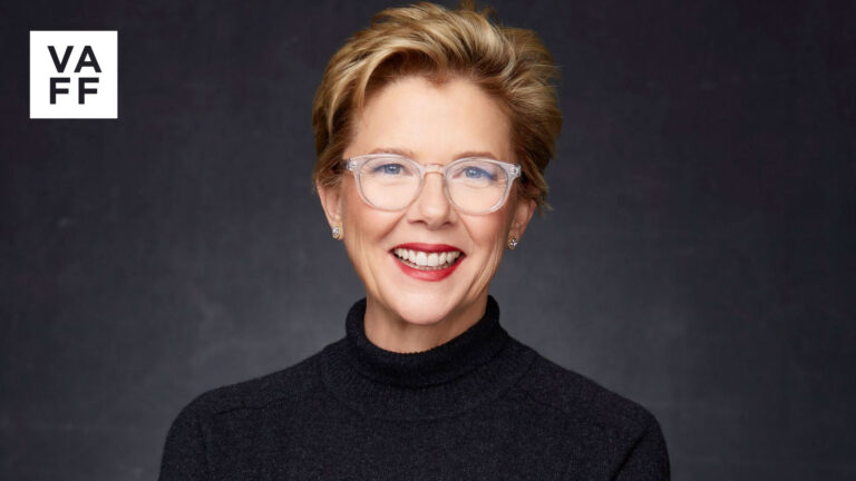 Annette Bening, smiling, wearing glasses and a black turtleneck sweater.