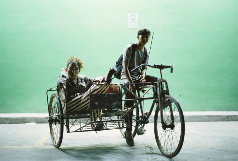Woman in sidecar, man on bike in front of green wall.