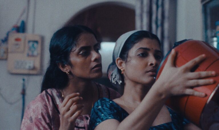 Two women in a scene from "All We Imagine as Light," one looking in a mirror.