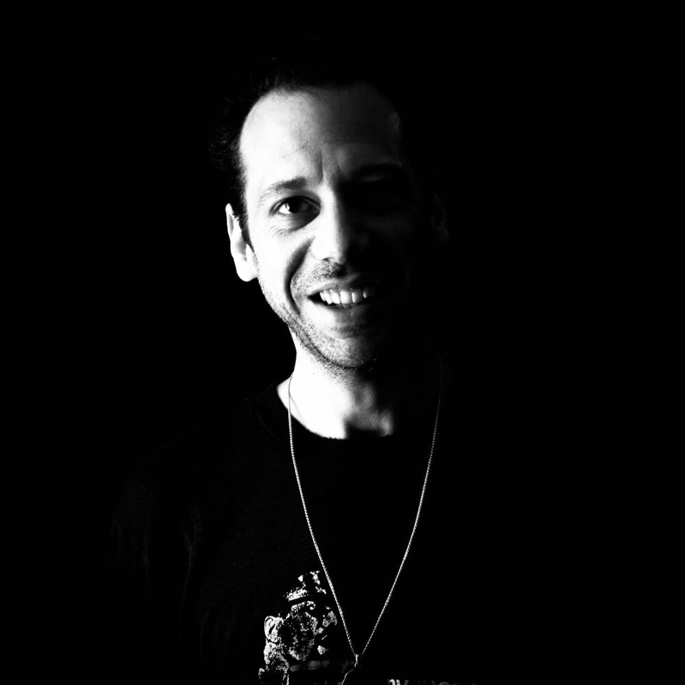 Portrait of Abel Okugawa smiling in a black t-shirt with a chain necklace.
