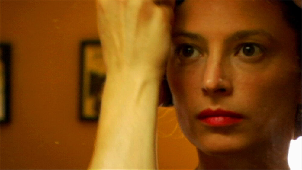 Close-up of an actress with red lipstick and intense gaze, arm raised.