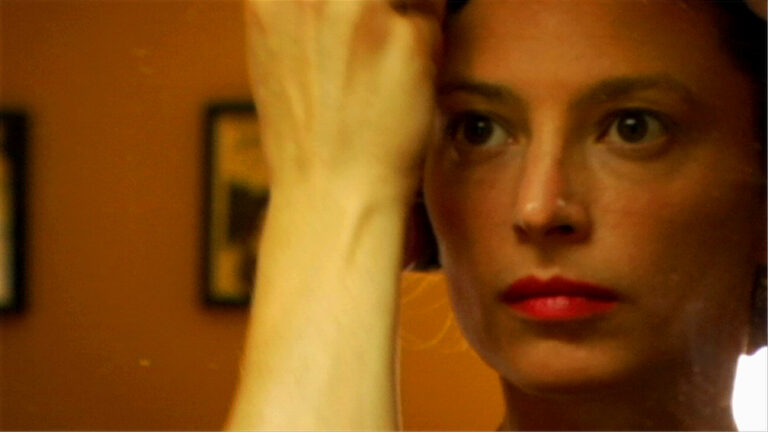 Close-up of an actress with red lipstick and intense gaze, arm raised.