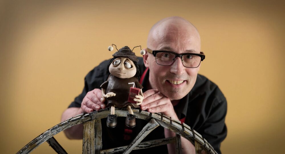 Adam Elliot poses smiling with a claymation character.