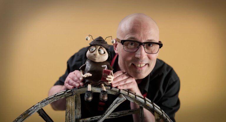 Adam Elliot poses smiling with a claymation character.