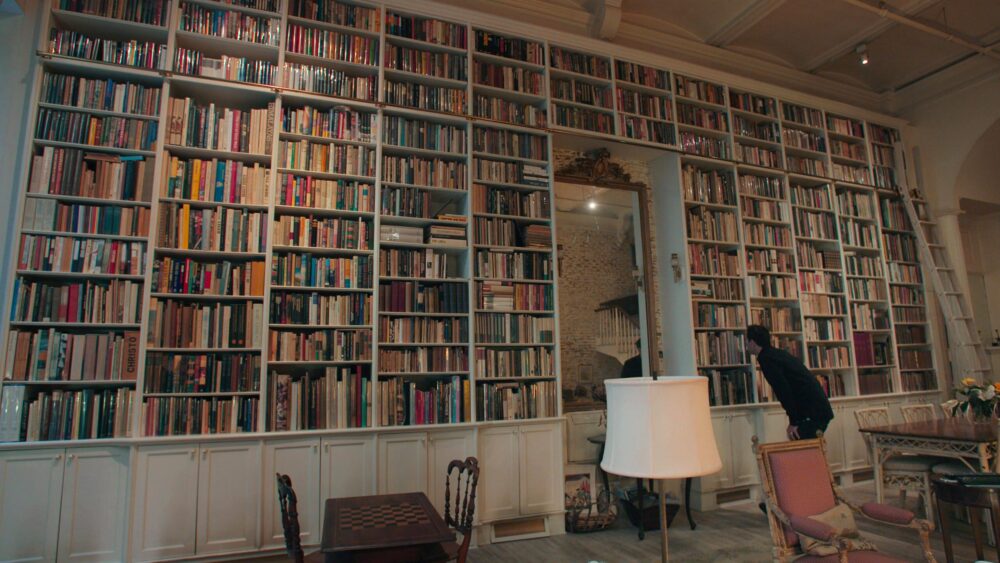 Floor-to-ceiling bookshelves filled with books, ladder, and a person looking at books.