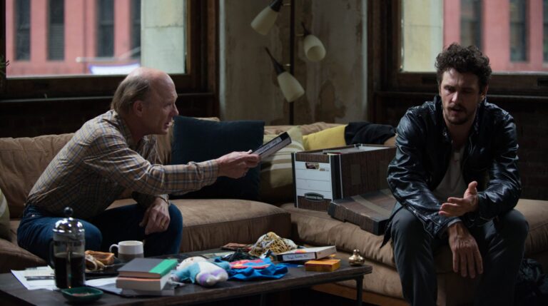 Scene from "The Adderall Diaries" movie: older man showing VHS tape to younger man.