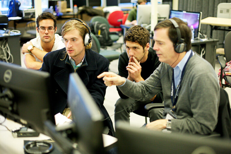 Team collaborating on the Adrenaline Film Project, reviewing footage on computer screens with headphones.