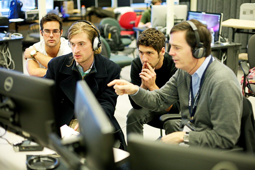 Team collaborating on the Adrenaline Film Project, reviewing footage on computer screens with headphones.