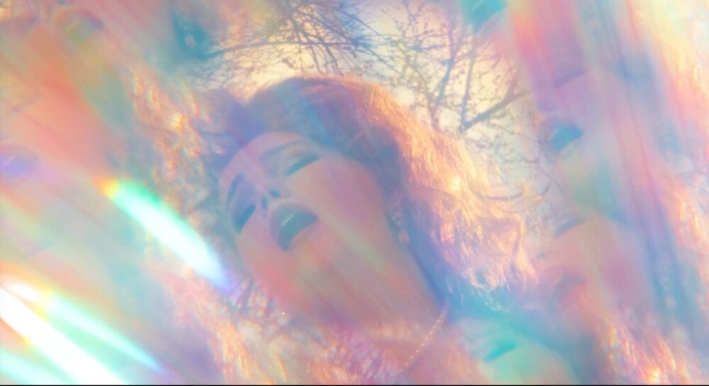 Dreamy portrait of Adrianne, bathed in rainbow light with trees in the background.