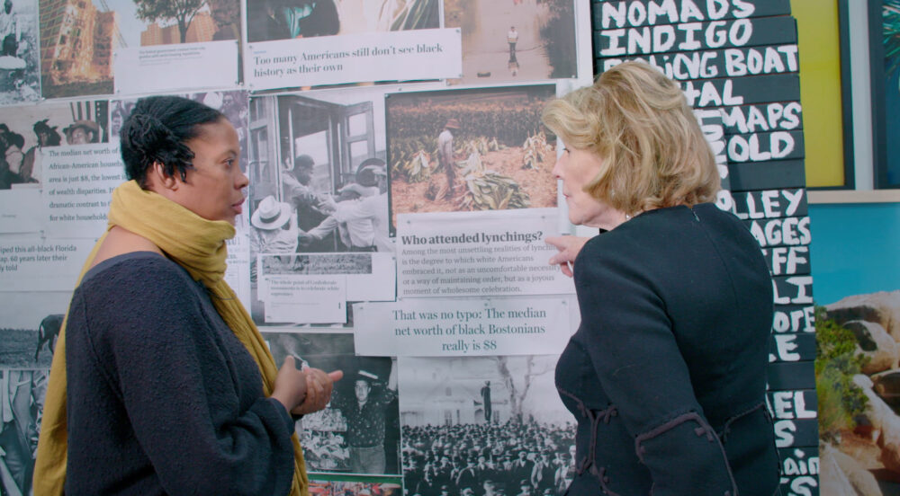 Two women discuss racial wealth disparities displayed on a wall.