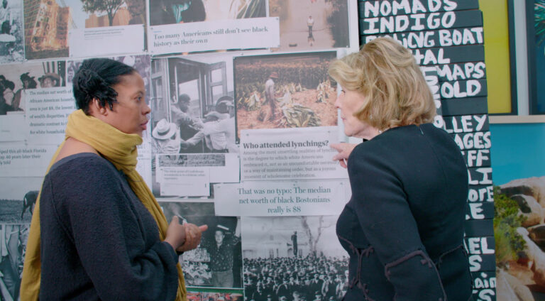 Two women discuss racial wealth disparities displayed on a wall.