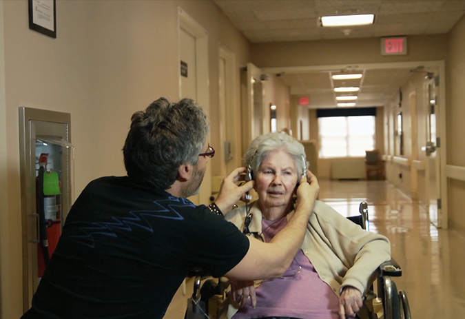 Man placing headphones on elderly woman in wheelchair in "Alive Inside" scene.