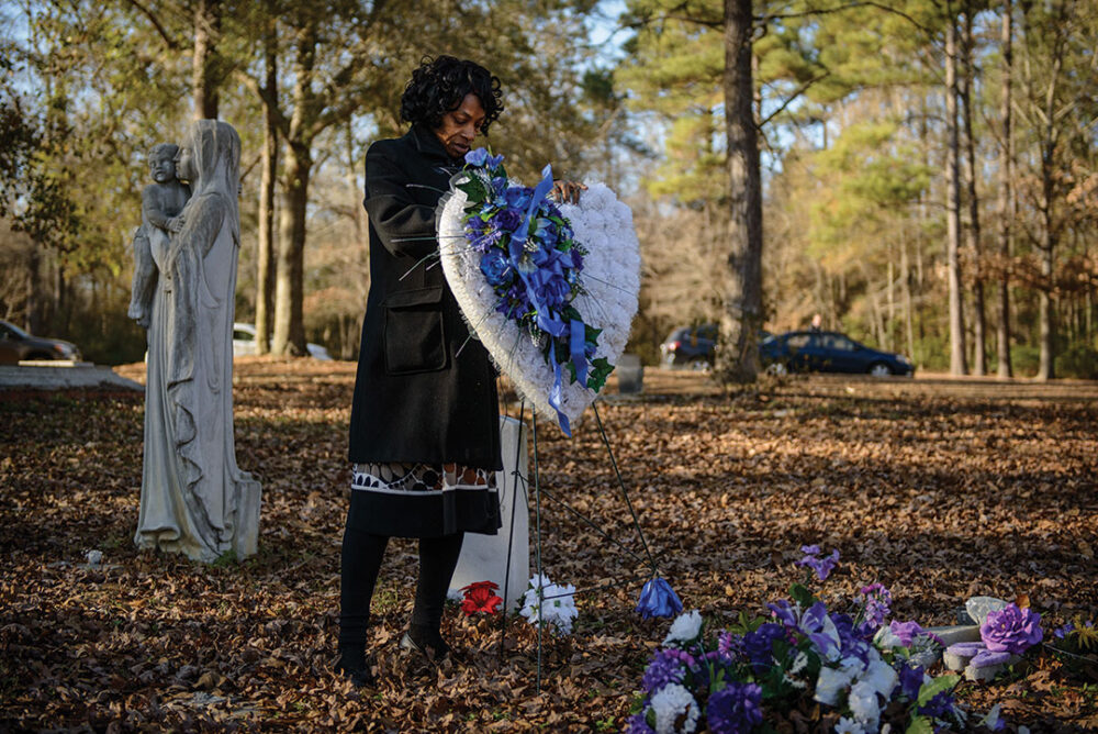 Woman places heart-shaped floral arrangement at gravesite.