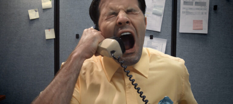 Frustrated office worker yelling into a telephone receiver in a cubicle.