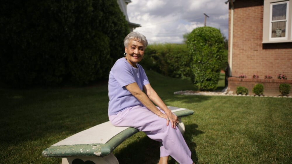 Senior woman sits on a bench in her yard, enjoying the outdoors.