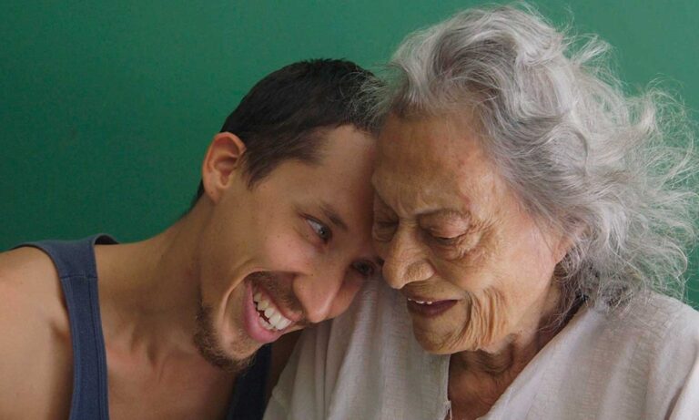 Young man smiling laying his head on the shoulder of an elderly woman.