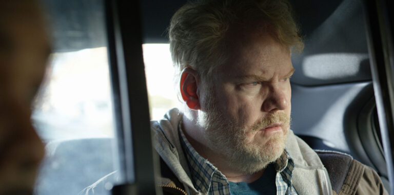 Jim Gaffigan in "American Dreamer" movie, looking concerned in the back of a car.