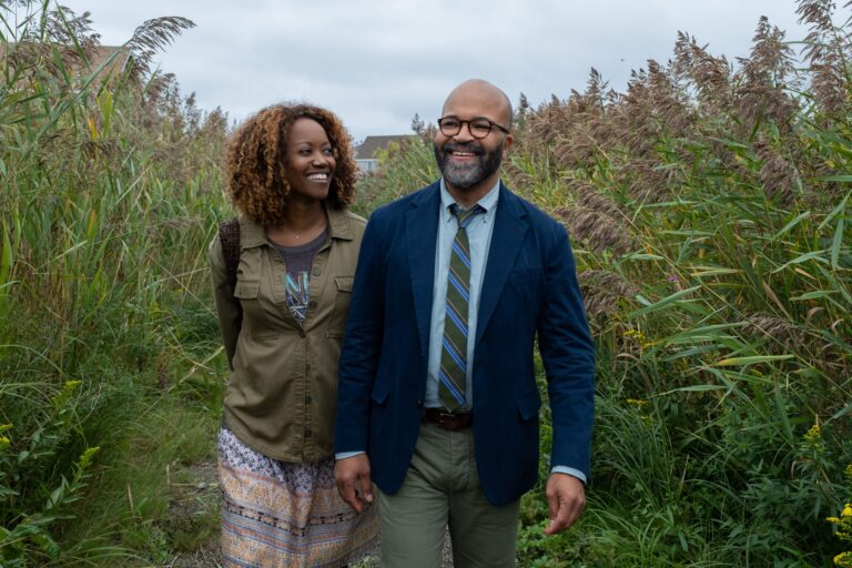Couple walking outdoors in "American Fiction" movie scene, smiling in a field.