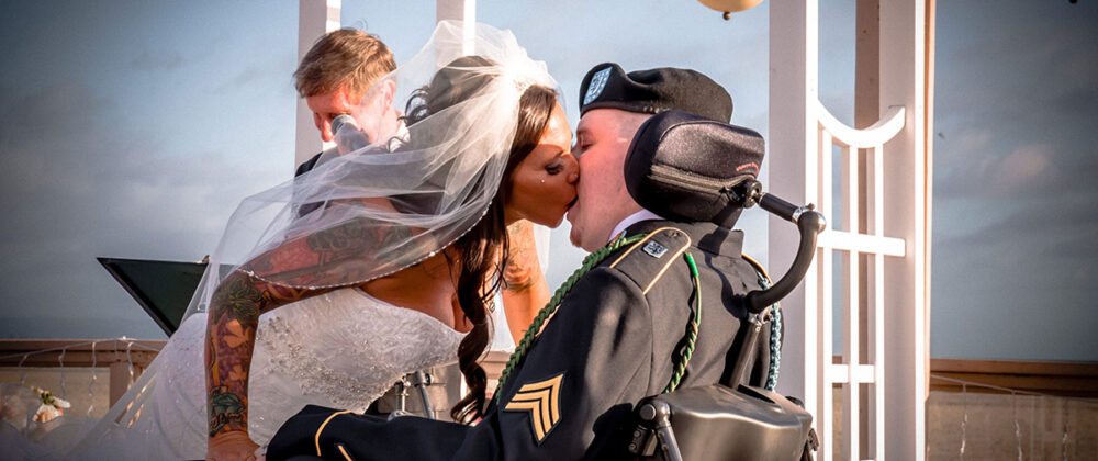 Bride kissing American veteran in wheelchair at wedding ceremony.
