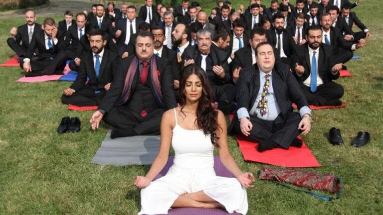 An Indian Father: Woman leads yoga session for businessmen in suits.