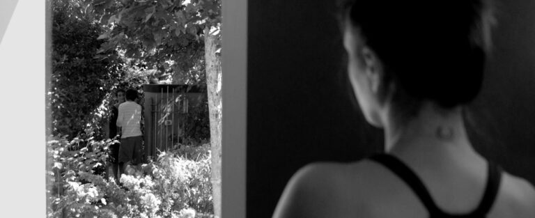 Short film still: Woman indoors, looking out at two people outdoors.