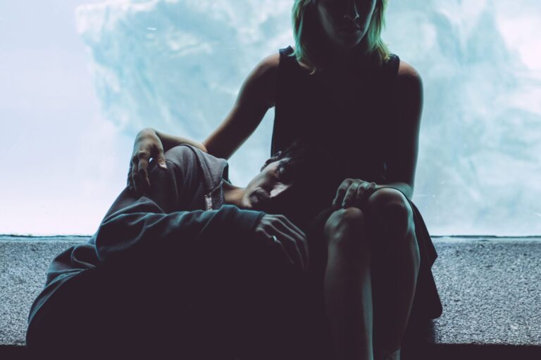 Person resting head on another's lap, sitting against a blue backdrop.