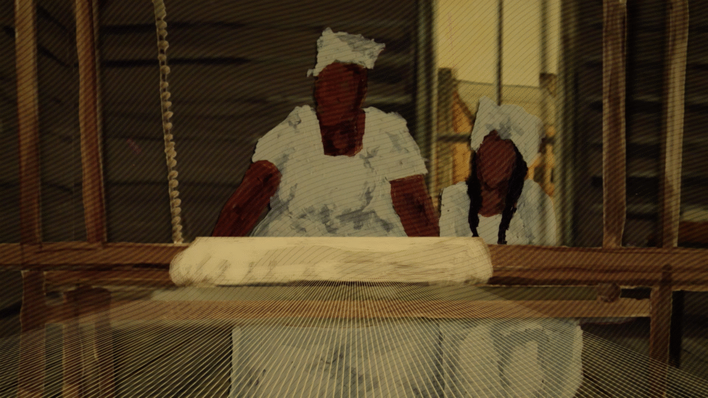 Two women in white caps work at a loom, weaving fabric.