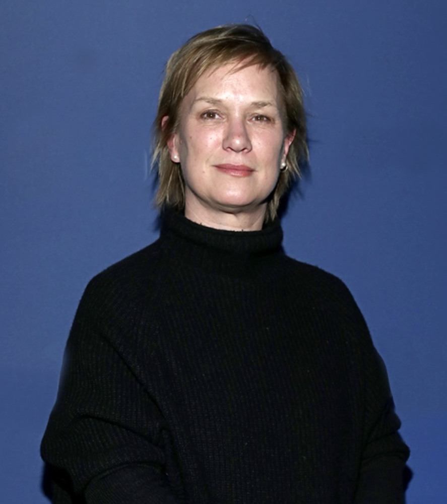 Anne Carey in a black turtleneck against a blue background.