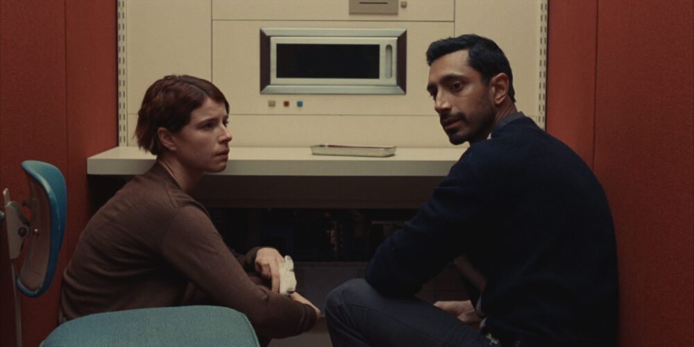 Riz Ahmed and Jessie Buckley in "Fingernails," seated in a sterile, minimalist setting.