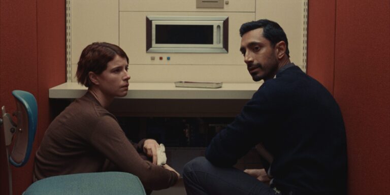 Riz Ahmed and Jessie Buckley in "Fingernails," seated in a sterile, minimalist setting.